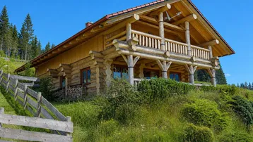 Traditionelles Blockhaus auf einem grünen Hügel mit Holzzaun und weitem Blick in die Natur.