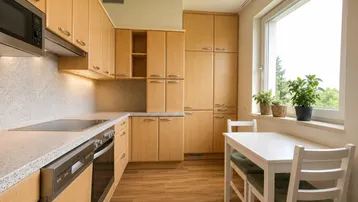 Funktionale Küche mit hellen Holzschränken, Esstisch und großem Fenster.