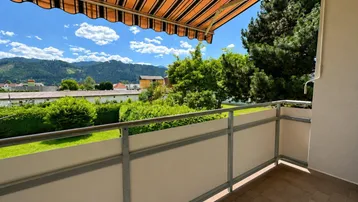 Sonniger Balkon mit Markise und weitem Blick auf die umliegende Landschaft und Berge.
