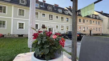 Blick auf die Fassaden der Wohngebäude von einem kleinen Gartenbereich mit Tisch und Blumen.