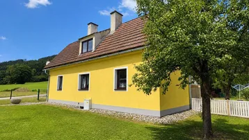 Gelbes Einfamilienhaus mit rotem Ziegeldach und grünem Garten unter blauem Himmel.