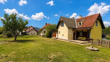 Großzügiger Gartenbereich mit Obstbaum, Sitzbank und Blick auf das gelbe Wohnhaus.