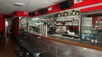 Geräumige Bar mit langer Theke, Barhockern und roten Wänden, ausgestattet für den Gastronomiebetrieb.