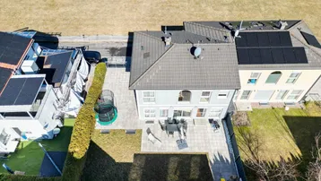Luftaufnahme des Hauses mit Garten, Terrasse und angrenzenden Feldern unter strahlendem Himmel.