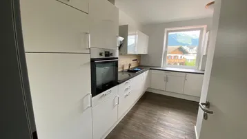 Moderne Einbauküche mit weißen Hochglanzfronten, integrierten Geräten und Bergblick aus dem Fenster.