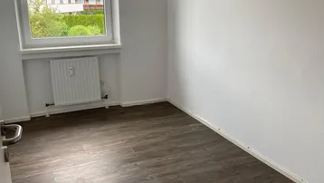 Gemütliches Schlafzimmer mit dunklem Laminatboden und einem Fenster, das einen grünen Ausblick bietet.
