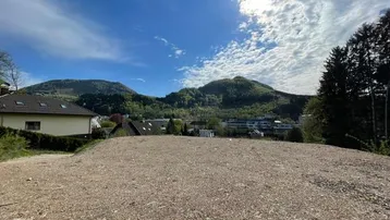 Weitläufiges Grundstück mit Schotterfläche und Blick auf die umliegende Berglandschaft unter blauem Himmel.