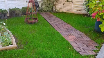 Gepflegter Gartenbereich mit Holzzaun, Ziegelweg und üppigem Grün, ideal zum Entspannen im Freien.