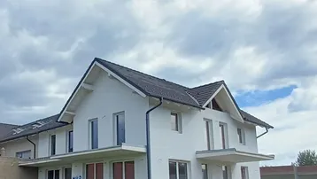 Modernes Einfamilienhaus mit weißer Fassade, Satteldach und zwei Balkonen, umgeben von Grünflächen.