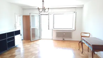 Helles Wohnzimmer mit Parkettboden, großen Fenstern und direktem Zugang zu einem Balkon.