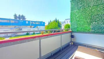 Balkon mit Holzboden und grüner Sichtschutzwand, bietet einen Blick auf die umliegenden Gebäude.