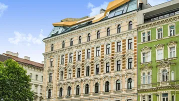 Ornate Fassade eines historischen Gebäudes mit moderner Dachaufstockung unter blauem Himmel.