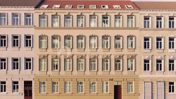 Mehrere Gebäude mit klassischer Fassade und parkenden Autos auf der Straße unter blauem Himmel.