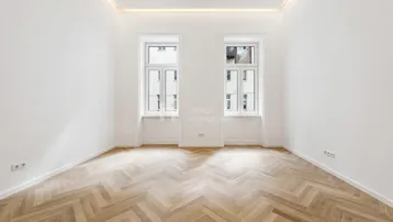Helles Zimmer mit elegantem Fischgrätparkettboden und zwei großen Fenstern.