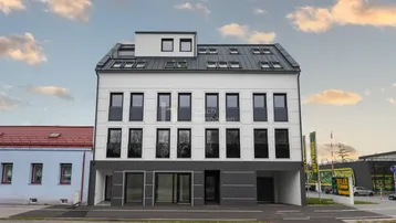 Moderne Wohnhausfassade mit weißem Putz, dunklen Akzenten und vielen Dachfenstern.