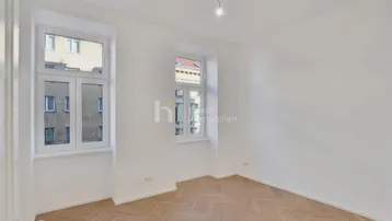Helles Zimmer mit Fischgrätparkett und weißen Wänden, bereit zur individuellen Gestaltung.