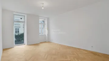 Helles Wohnzimmer mit Fischgrätparkett und Zugang zu einem kleinen Balkon.