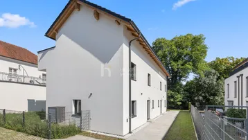 Seitenansicht eines modernen Neubaus mit weißer Fassade und gepflegtem Außenbereich unter blauem Himmel.