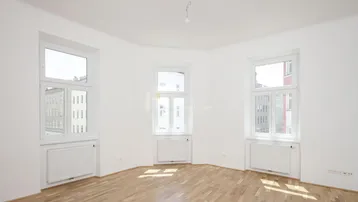 Helles Zimmer mit Parkettboden und mehreren Fenstern, ideal als Wohn- oder Schlafbereich.