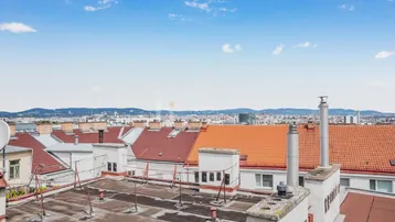 Weitblick über die Dächer der Stadt mit Bergen am Horizont unter blauem Himmel.