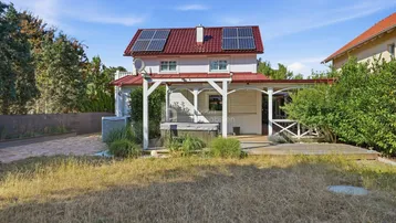 Großer Gartenbereich mit Rasenfläche, Holzterrasse, Whirlpool und einem Haus mit Solaranlage auf dem Dach.