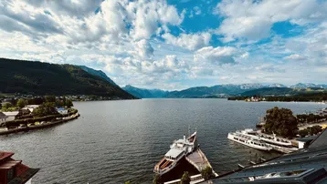 Atemberaubender Blick auf den See mit Bergen und Booten unter einem weiten Himmel.