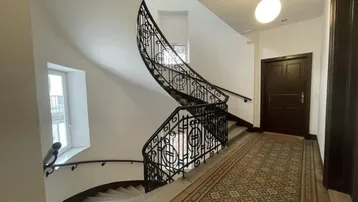 Eindrucksvolles Treppenhaus mit kunstvollem schmiedeeisernem Geländer und gemusterten Fliesenböden in einem Altbau.
