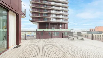 Große Holzterrasse mit Liegestühlen und Blick auf das moderne Hochhaus und die Umgebung.