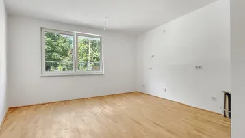 Heller, leerer Raum mit weiß gestrichenen Wänden und hellem Holzparkettboden, mit Blick ins Grüne.