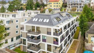 Modernes Mehrfamilienhaus mit Balkonen und Dachfenstern in einer grünen Wohngegend am Hang.