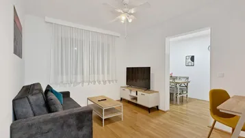 Helles Wohnzimmer mit bequemer Couch, Fernseher und Zugang zum Essbereich.