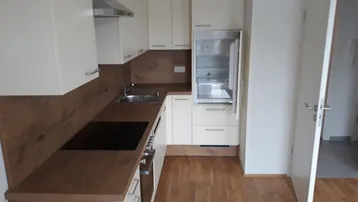 Moderne Einbauküche mit hellen Schränken, Holzoptik-Arbeitsplatten und integrierten Geräten.