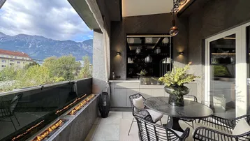 Großer Balkon mit Sitzgelegenheiten, Esstisch und Kamin mit Bergblick.