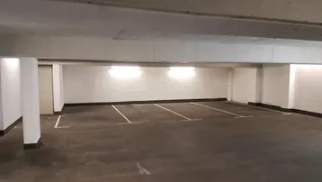 Tiefgarage mit mehreren markierten Stellplätzen, künstlicher Beleuchtung und Betonboden.