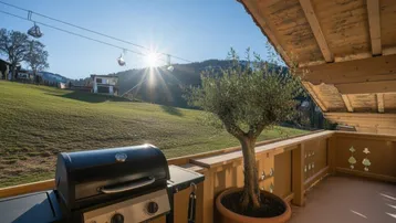 Sonniger Balkon mit Grill und Blick auf die Skipiste und die umliegende Berglandschaft.