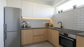 Moderne Küche mit hellen Holzfronten, weißen Oberschränken und integrierten Geräten.