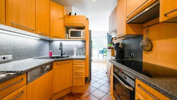 Helle Küche mit Holzschränken, dunkler Arbeitsplatte und Terrakottafliesen, mit Zugang zum Außenbereich.