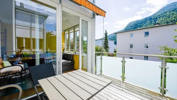 Heller Balkon mit Holzboden, Esstisch und weitem Blick auf die Berge.