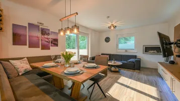 Helles Wohn- und Esszimmer mit Holzboden, gemütlicher Sitzecke und Zugang zum Balkon.