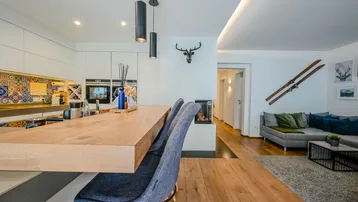 Offener Wohn- und Essbereich mit moderner Küche, Holzboden und Kamin, dekoriert mit alpinen Elementen.