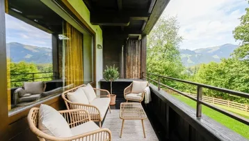 Möblierter Balkon mit Rattanmöbeln und atemberaubendem Bergblick in die grüne Landschaft.