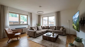 Helles Wohnzimmer mit großem Ecksofa, Holzboden und Blick ins Grüne durch die Fenster.