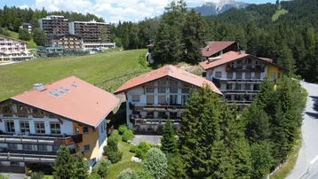 Luftaufnahme von traditionellen Gebäuden mit roten Dächern in einer bergigen, bewaldeten Landschaft.