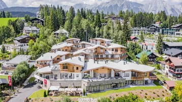 Luftaufnahme eines modernen Apartmentkomplexes in alpiner Umgebung mit Bergblick und viel Grün.