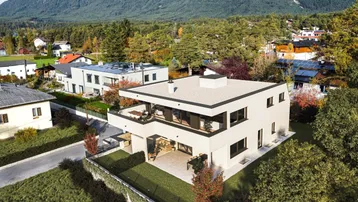 Moderne Villa mit Flachdach und Bergblick, umgeben von grüner Landschaft und Bäumen.