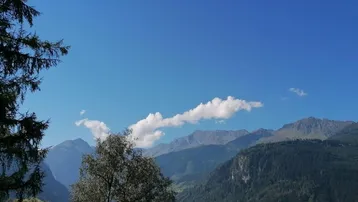 Malerischer Bergblick unter blauem Himmel mit einigen Wolken und Bäumen im Vordergrund.