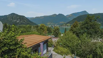 Blick über die Dächer und grüne Landschaft zum See und den umliegenden Bergen.