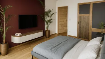 Modernes Schlafzimmer mit Holzboden, einer Akzentwand in Bordeauxrot und integriertem TV-Bereich.