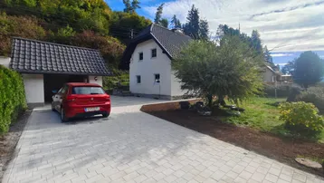 Einfamilienhaus mit gepflasterter Auffahrt, Garage und umgebender grüner Landschaft.