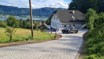 Modernes Einfamilienhaus mit gepflasterter Auffahrt und malerischem Seeblick in grüner Umgebung.